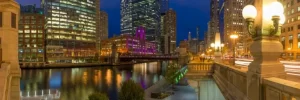 Chicago riverwalk at night with brightly lit buildings and a bridge representing limo service Chicago.